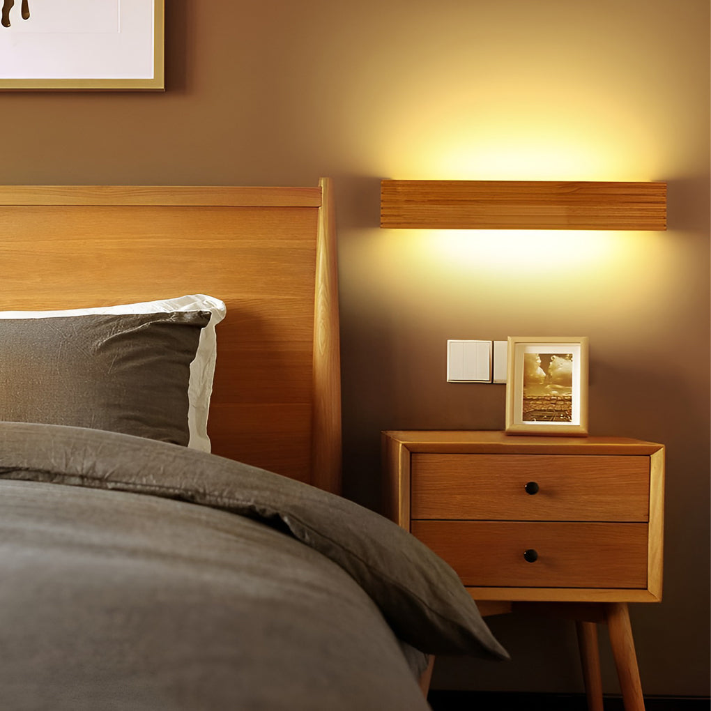 Wooden wall lamp mounted above a bedside table, offering gentle illumination for a modern bedroom.